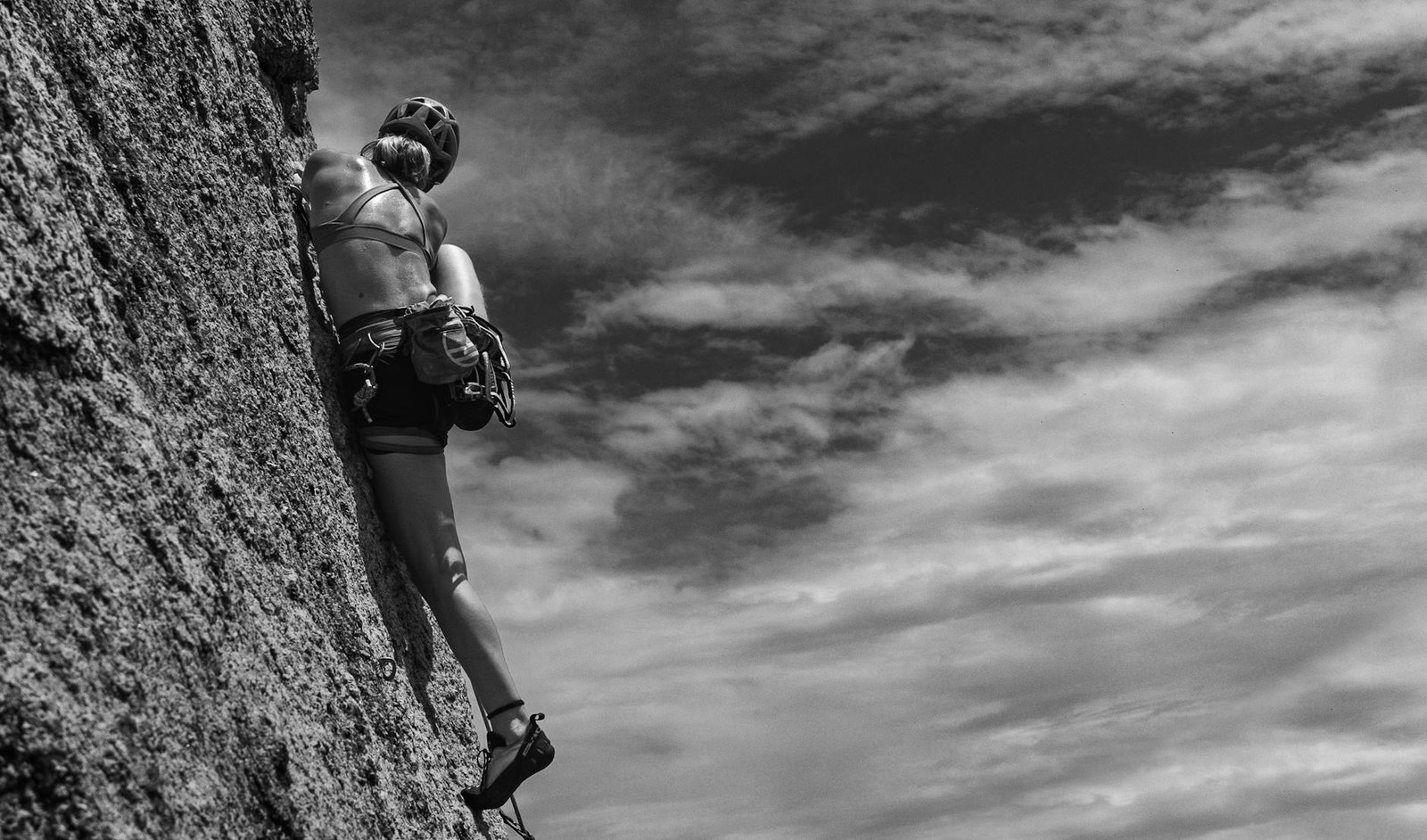 woman rock climbing under clouds in black and white