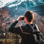 man using black binoculars near forest trees at daytime