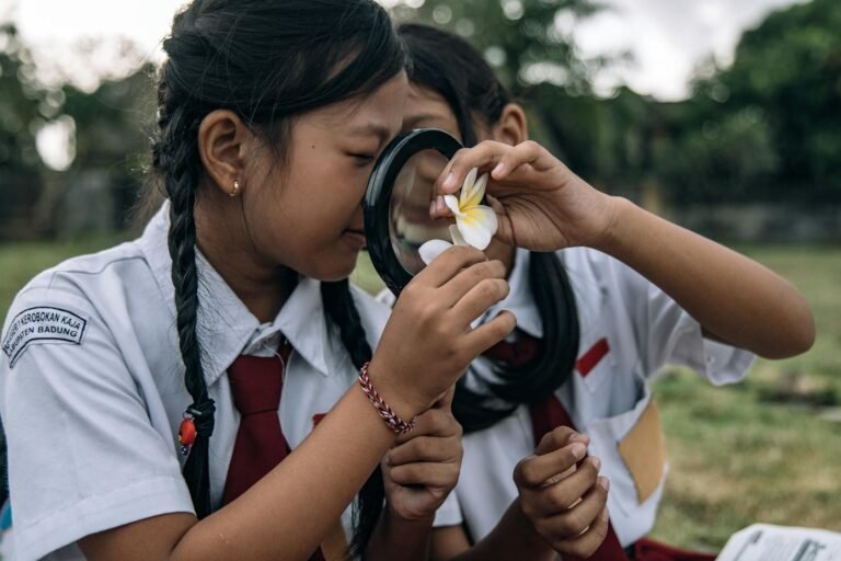 two girls in school uniforms using a magnifying glass