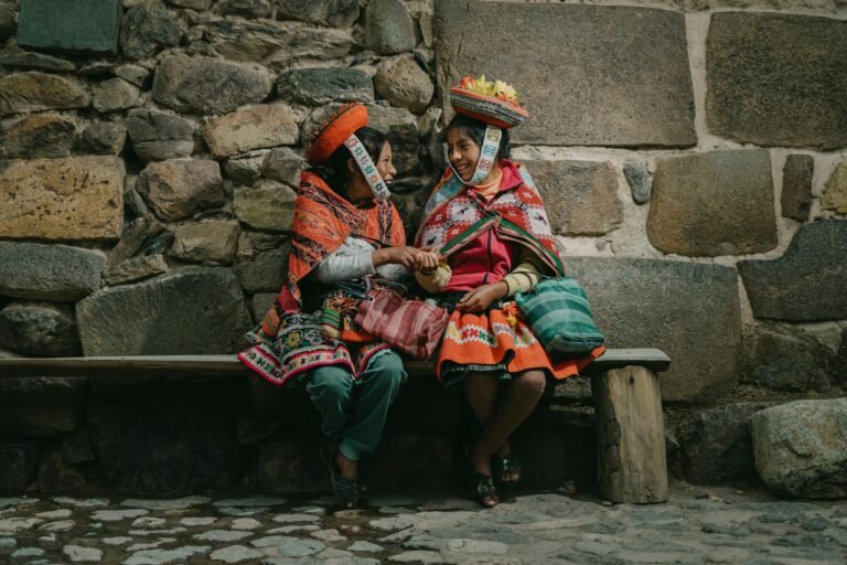 peruvian girls wearing traditional clothing sitting on a bench by a wall