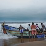 fishermen towing boat on sea shore