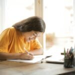 woman in yellow shirt writing on white paper