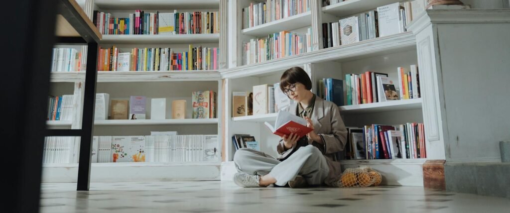 man in white dress shirt sitting on floor beside book shelf