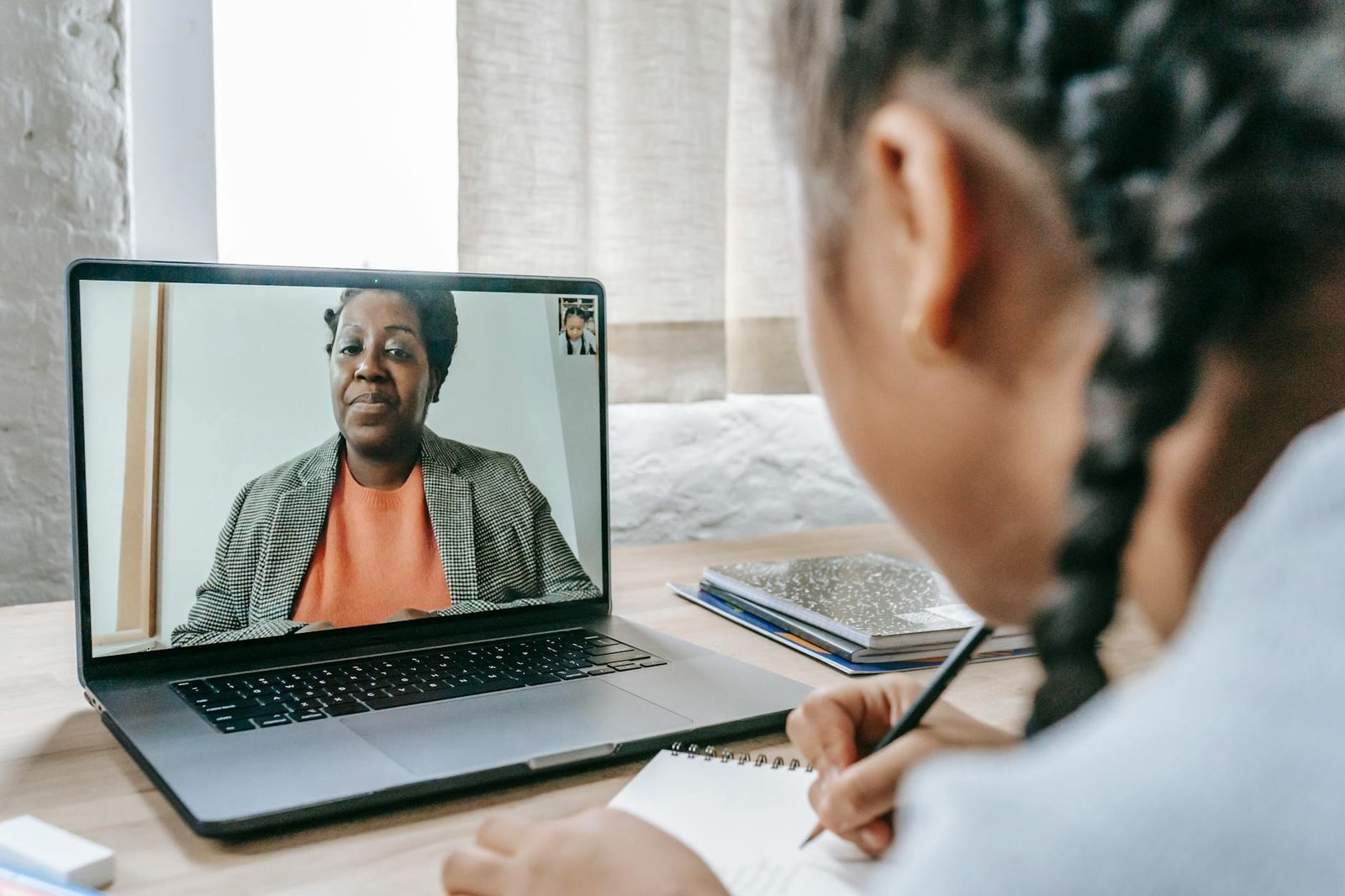 diligent ethnic girl writing notes while tutor giving lesson online
