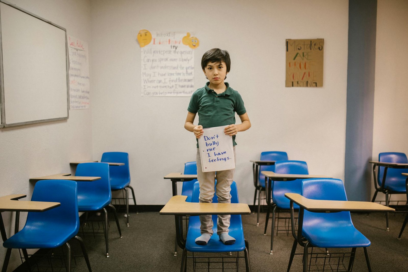boy standing on blue chair while holding a message against bullying