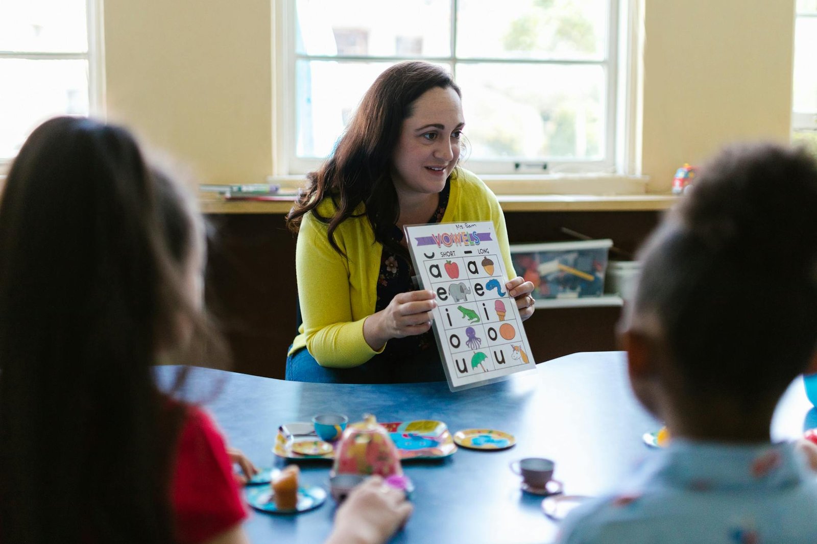 woman in yellow long sleeve shirt showing letters on a book to kids