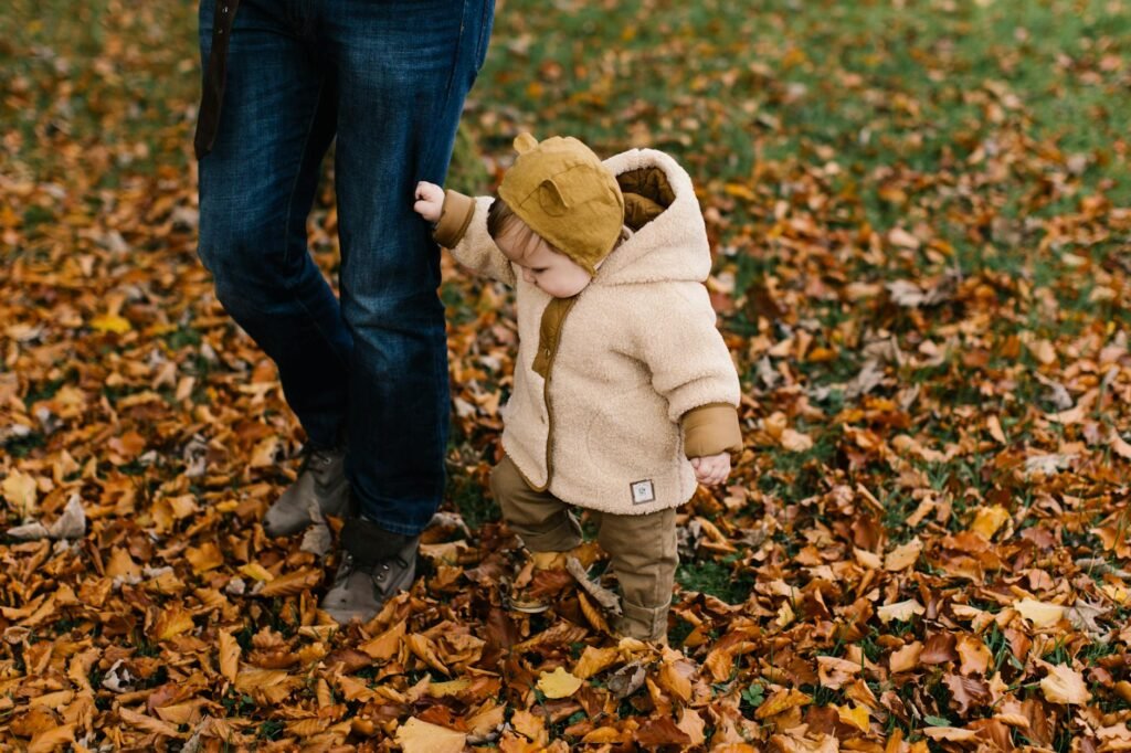child in beige hoodie and brown denim jeans standing on dried leaves